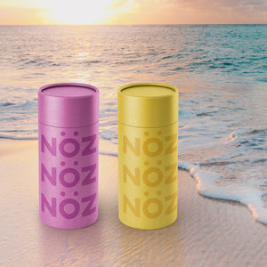 NOZ sunscreen tubes in purple and yellow on the beach